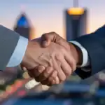 A close-up shot of a handshake between a male registered agent and a businessman, with a blurred cityscape of Birmingham, Alabama, at dusk in the background, conveying trust and partnership.