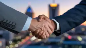 A close-up shot of a handshake between a male registered agent and a businessman, with a blurred cityscape of Birmingham, Alabama, at dusk in the background, conveying trust and partnership.