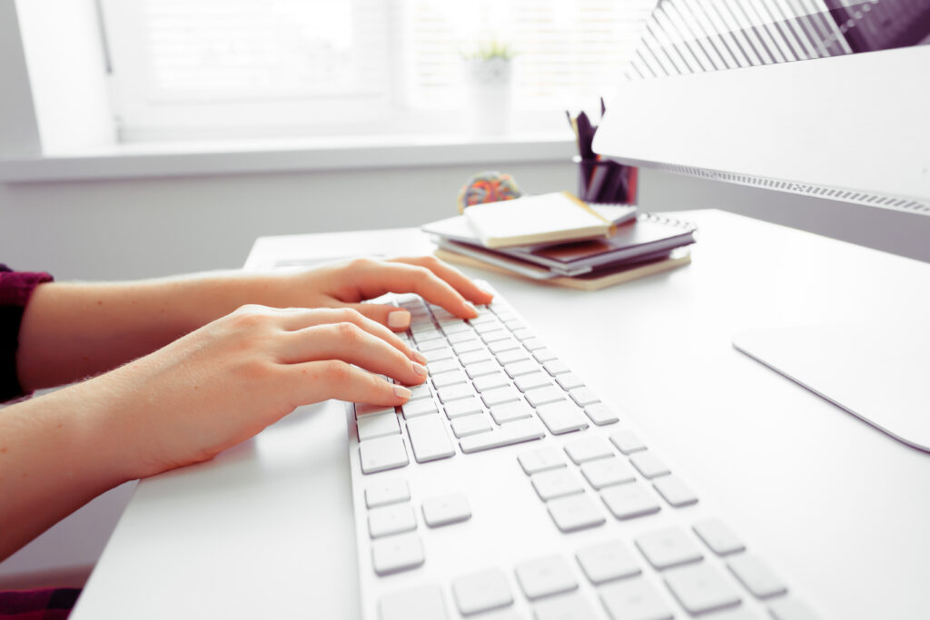 Hand typing on an office desk: registered agent technology.